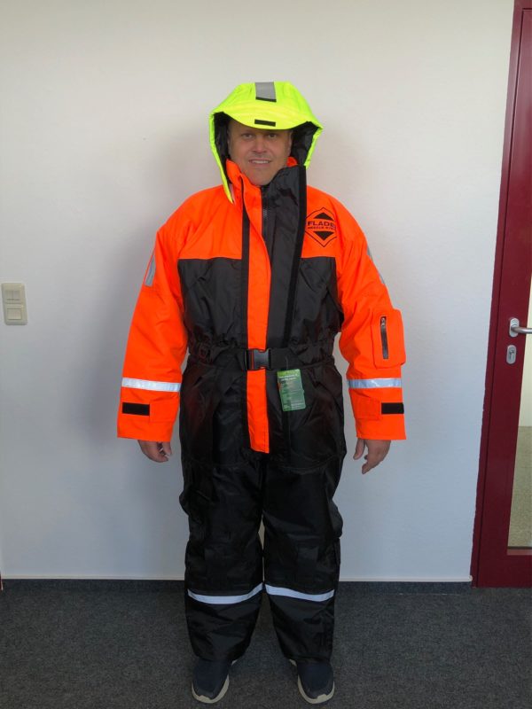 Person in auffälligem, orangem und schwarzem Überlebensanzug mit gelber Kapuze und reflektierenden Streifen.